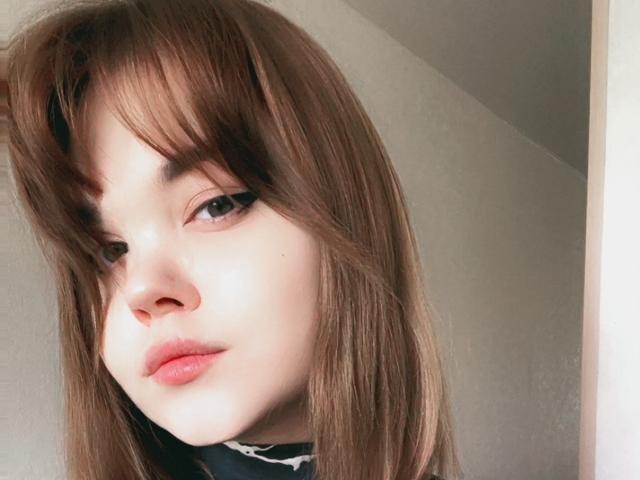 LettyRussum has light skin, brown hair with bangs, and pink lips. She's looking slightly to the side with a subtle, confident smile. Her makeup is subtle and natural.