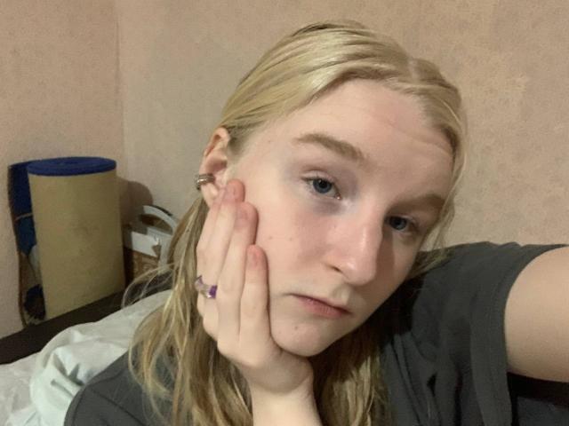 Hyacinth Bellin, met bleke huid, blond haar en blauwe ogen, leunde met haar hoofd op haar hand, zag er moe uit, droeg een grijze trui en had een paarse ring om haar vinger..
