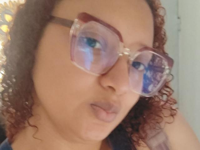 VioletaSwitch has curly red hair, wearing pinkish-tinted glasses with reflective blue eyes, and is pouting with slightly parted pinkish-brown lips. Her tan skin is visible.