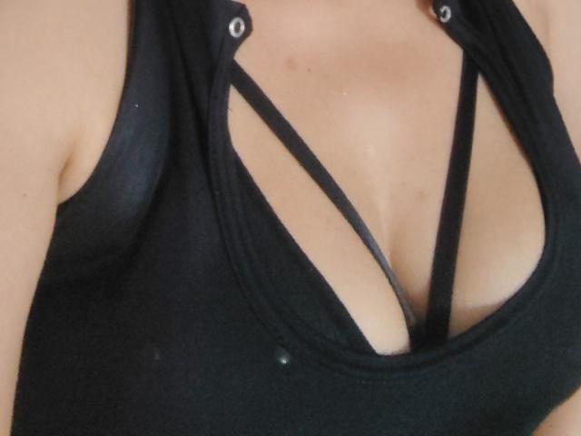 VioletaSwitch's black tank top with strappy design, exposing her large, cleavage-filled tits. Black straps cross over her chest, highlighting her tan, smooth skin.