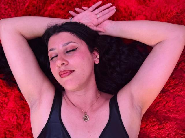LunaDamasco with arms above head, black tank top, red shaggy background, eyes closed, dark hair, pinkish skin, subtle makeup, necklace, relaxed, slight smirk, visible armpit.