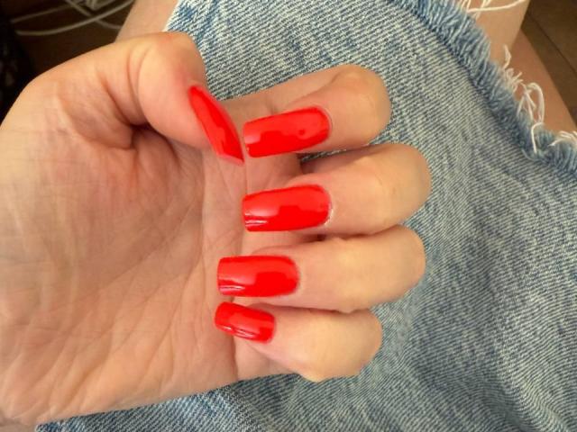 La main de FellDivain, avec ses ongles acryliques longs, pointus et rouges brillants, repose sur une surface en tissu bleu, texturée et effilochée..