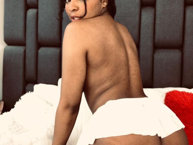 LisaMendez is topless with her back to the camera, wearing a white skirt that reveals her ass. She has dark skin and is looking over her shoulder.