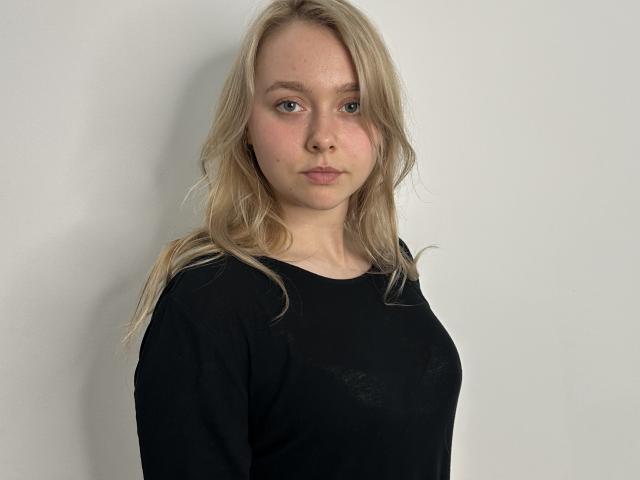 Retta Gundry heeft blond, golvend haar en draagt een zwarte blouse. Haar borsten zijn klein, en ze heeft een neutrale, lichtjes fronsende uitdrukking. Ze staat tegen een effen witte muur..