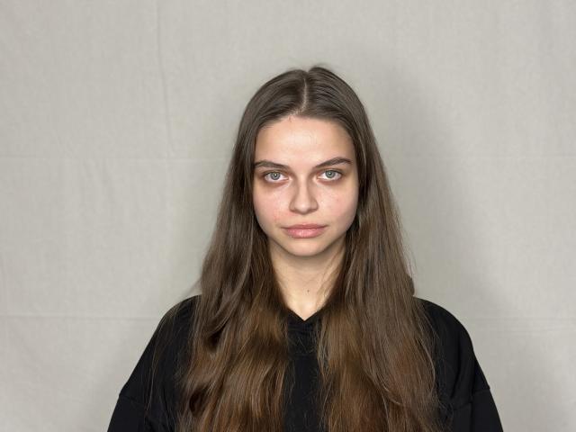 NormanSundberg has long brown hair, fair skin, and blue eyes, wearing a black shirt, with a neutral expression, looking straight at the camera.