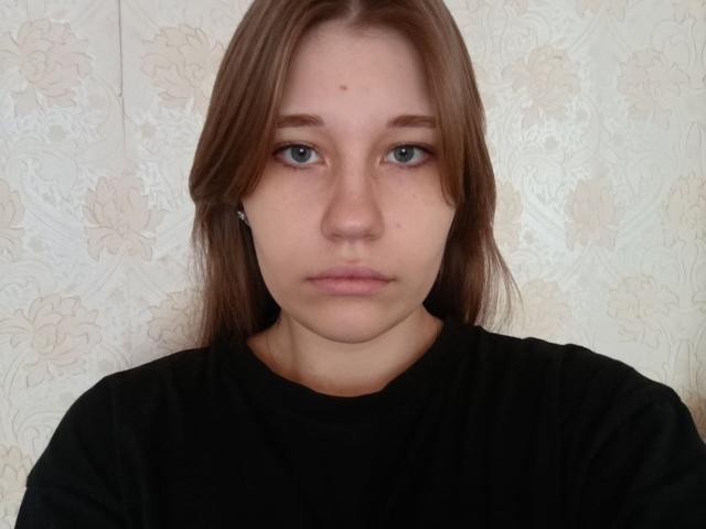RachellVanschoiack tem uma expressão séria, cabelo castanho, olhos azuis e pequenas espinhas na testa. Ela está vestindo uma camisa preta e olhando diretamente para a câmera..