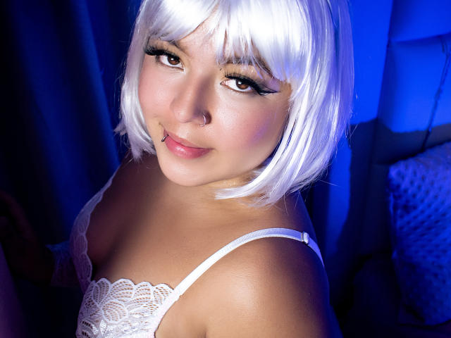 BarbaraHoneyy with white bob, eyeliner, and nose ring, wearing lace top, smiling, showing her tits, blue light, shiny skin, lip piercing, cute, sexy.