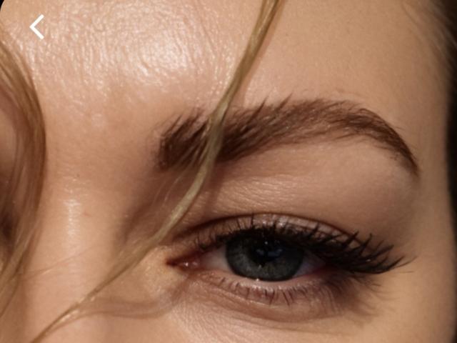 GladisBelle's blue eye with long, thick black eyelashes, a well-groomed brown eyebrow, and blonde hair partially covering her face. Her skin is smooth and fair.