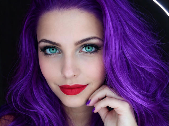 GoddessNix tem cabelos roxos vibrantes, olhos azuis e batom vermelho. Ela está sorrindo, com a mão perto do rosto, e suas unhas roxas contrastam com sua pele clara..