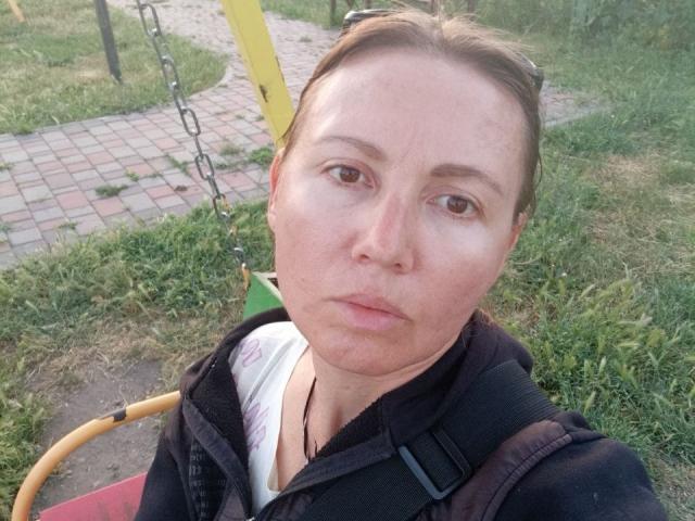 ZoyaPask has a puffy, pale face with brown eyes, a slight double chin, and a serious expression. She's wearing a black vest and a white shirt with pink text.