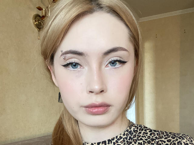AmeliaBonneville has blonde hair, blue eyes, and a small facial piercing above her right eyebrow. She's wearing bold black eyeliner and a leopard print shirt.