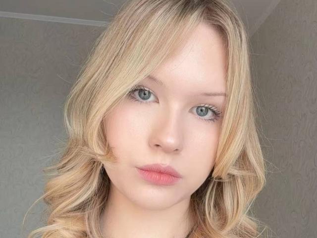 EllamaeRaugust has blonde, wavy hair, light skin, blue eyes, and pink lips. Her face is centered in the image, looking directly at the camera.