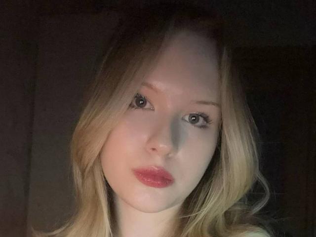 EllamaeRaugust has light blonde hair, pale skin, and pink glossy lips. Her blue eyes are slightly upturned, and she's looking directly at the camera.