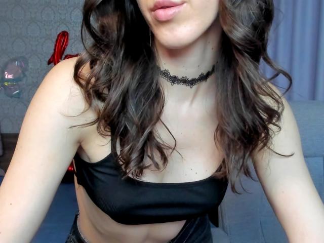 Rozalin with wavy brown hair, wearing a black choker and strapless black top, showing her small tits and slightly visible belly button. Soft pink lips, subtle makeup.