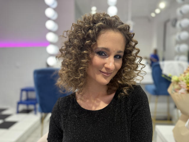 MichelleHotX69 with curly blonde hair, wearing a black sparkly top, smiling at the camera. Boobs not visible, ass not visible, tits not visible, pussy not visible.