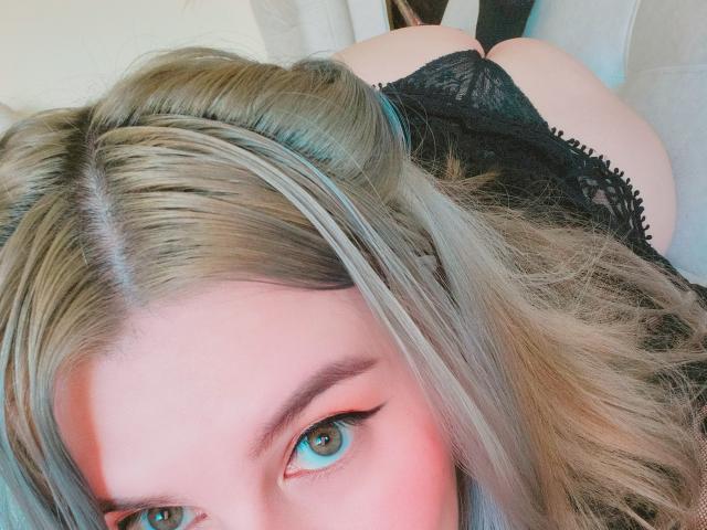 Akkanee's blue eyes looking up, blonde hair with blue highlights, wearing black lace panties, butt raised, soft pink blush on cheeks, lying down, slightly out of focus.