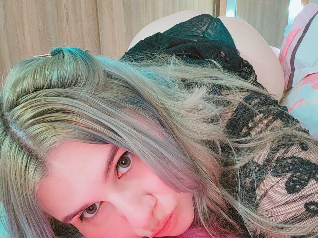 Akkanee with blonde hair, blue eyes, and pink blush, wearing black lace, on knees, showing bare ass, looking at camera. Her lips are slightly parted, her expression is relaxed.