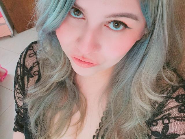 Akkanee with blue eyes, pink lips, and blue-gray hair, wearing a black lace top, looking up with a slight smile. Her tits are partially visible through the lace.