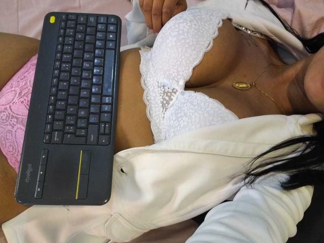 I seni di Clair Bennet, in un reggiseno di pizzo bianco, con perizomi di pizzo rosa, e un laptop nero poggiato sullo stomaco, con una camicia bianca aperta e una collana d'oro..