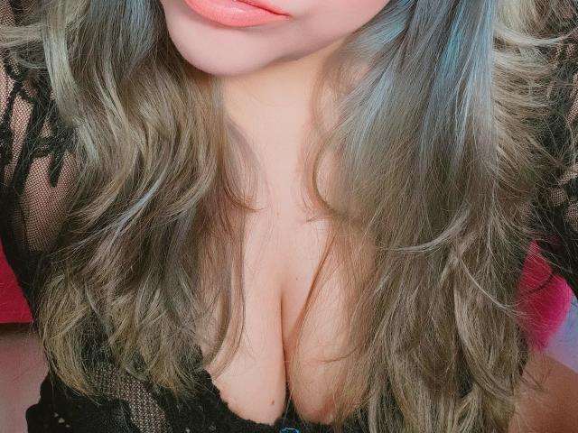 Akkanee's tits are showing through her black lace top with wavy, grayish-blue hair and pink lipstick. Her cleavage is prominent and her skin is light.