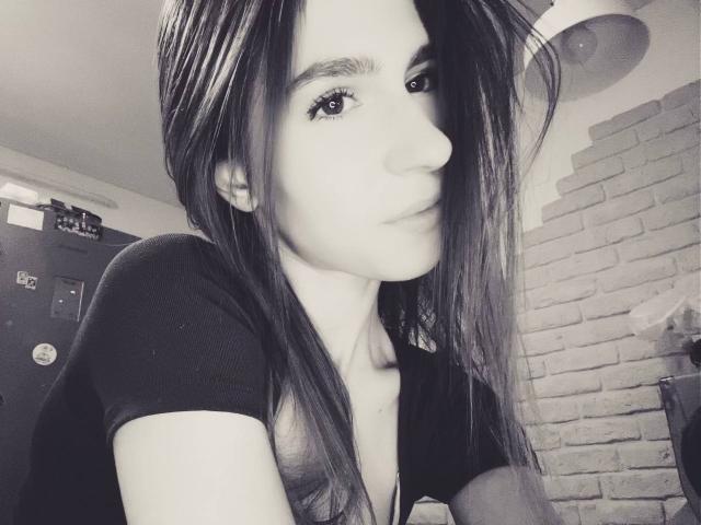 BridgettCatignani with long, straight hair, wearing a black shirt, has a small nose and slight smile, looking to the side in a grayscale selfie. Boobs partially visible.