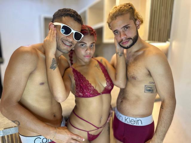 Three SauvageSexeADS in a kitchen. SauvageSexeADS with red hair and tits in a red lace bra and panty set, flanked by two shirtless guys in Calvin Klein underwear.