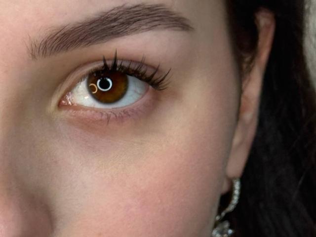 MeganCarlson's brown eye with long black eyelashes, thick brown eyebrows, and fair skin. Her ear with a silver earring is partially visible on the right.