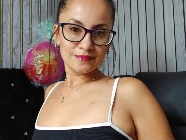 SolaraDubois with glasses, pink lipstick, black tank top, small tits, dark skin, brown hair in a ponytail, holding a colorful, wrapped ball on a black, tufted sofa.