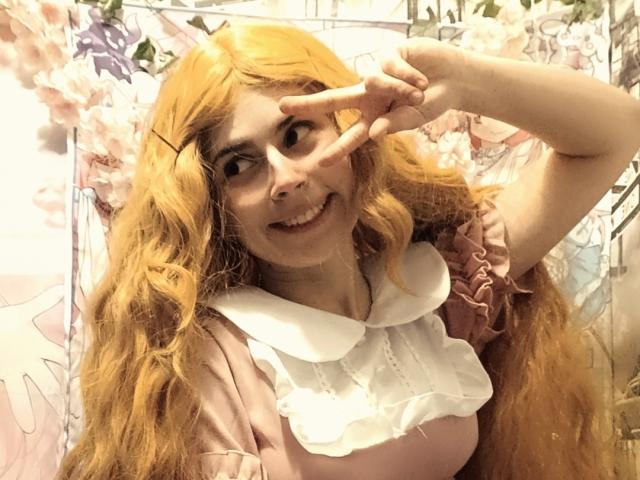 MireilleSpotwood with long, wavy orange hair, pink dress, white ruffled collar, smiling, making a peace sign with her right hand, showing cute, nerdy, and playful vibe.