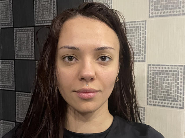 Candida Bardill hat feuchtes, braunes Haar, hellbraune Augen, ein Nasenpiercing und trägt ein schwarzes Hemd. Ihre Haut ist glatt mit einem leichten Glanz. Ihr Hintern ist nicht sichtbar..