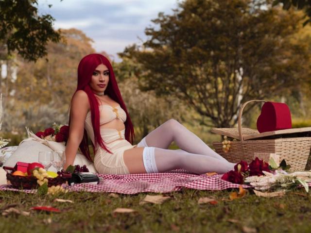 TifanySuarez with red hair, white lace lingerie, and thigh-high stockings, sitting on a red checkered blanket, surrounded by a picnic with a red hat and rose petals.