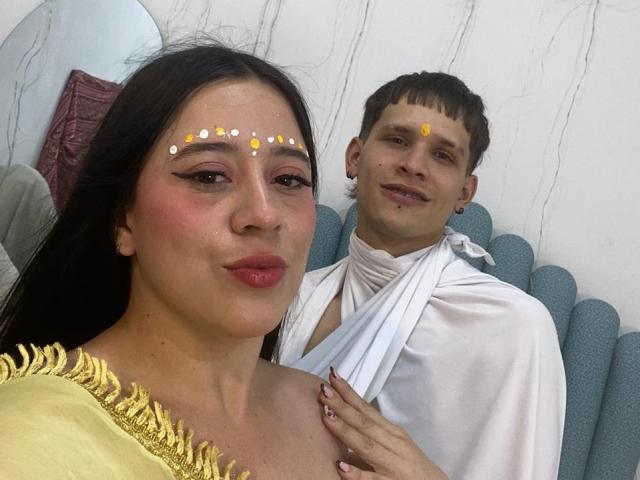 AnjaliRohan with dark hair, red lipstick, and white dots on forehead, wearing a yellow top, next to a man with brown hair, white cloth, yellow dot on forehead.