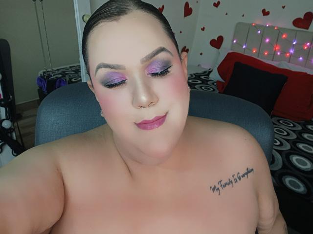 GiiannaMorrys, sin ropa en la parte superior, con sombra de ojos morada, colorete rosa y lápiz labial rosa, tiene un piercing en la nariz y un tatuaje en el hombro derecho que dice "Mi corazón está vacío".."