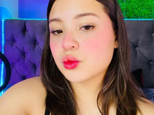 RyanNPricee's puffy pink lips are slightly puckered in a kiss, with red lipstick and rosy cheeks. She has dark brown hair, light skin, and brown eyes.