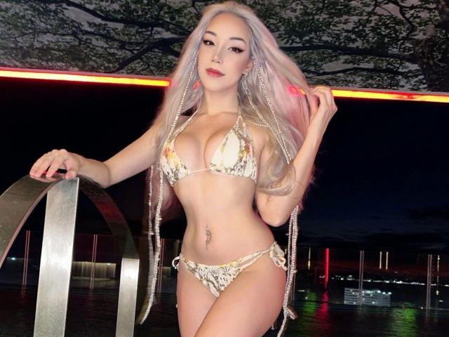 Icyvai-hot mit langen, pinkfarbenen Haaren, trägt einen glitzernden Bikini, zeigt ihre Brüste und ihren Hintern, steht nachts an einem Metallgeländer und hält ihre Haare..