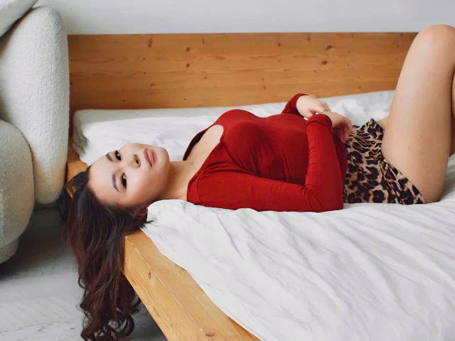 Sakura-hot lying on a bed, wearing a red long-sleeve top and leopard print shorts, with her tits slightly visible, her ass up, and her head turned towards the camera.