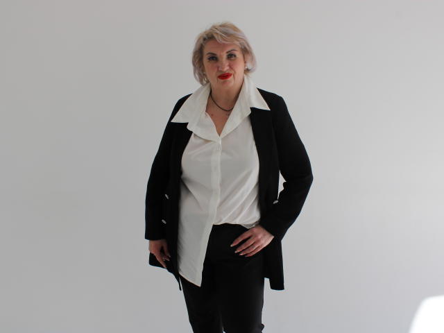 RenataDaster, blonde, wearing black jacket, white shirt with collar, black pants, standing, hand on hip, red lipstick, slight smile, white background, confident, sexy, busty.