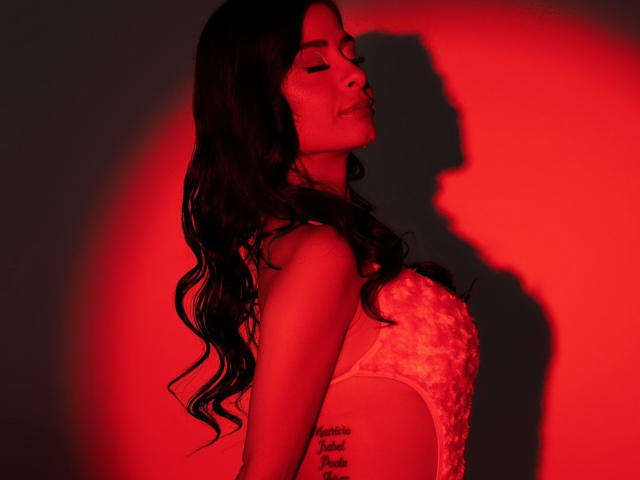 Shirley Siegel, con cabello negro, vestido negro, sosteniendo una pelota naranja, subiendo escaleras de mármol, usando zapatos de tacón alto negros, barandilla dorada, globos florales rojos y naranjas, paredes de madera oscura..