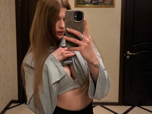 Barabara Wedemeyer, con i suoi lunghi capelli castani, solleva una maglietta grigia per mostrare i suoi piccoli seni, indossando un reggiseno nero, e si scatta un selfie allo specchio con il suo telefono..