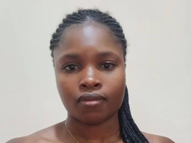 Zilpah's dark brown face with braided black hair, medium brown skin, and small, round brown eyes, showing a slight, confident smile and a simple gold necklace.