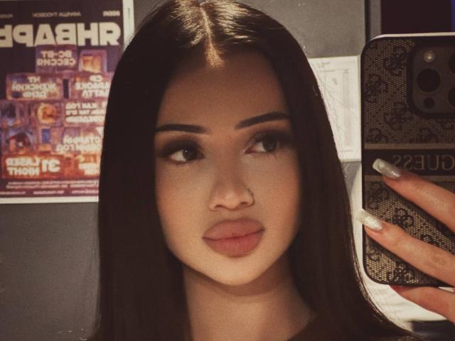 ShirleySiegel has long brown hair, full lips, and a nose ring, taking a selfie with her phone, showing off her white nails, looking to the side.