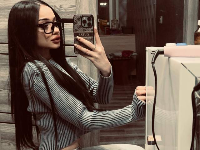ShirleySiegel with long black hair, glasses, striped crop top, holding phone in mirror selfie, showing small tits, standing in bathroom, holding toilet paper.