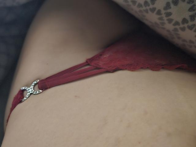 La tanga roja de encaje de SunshineTwo, con un clip plateado con forma de mariposa, muestra su trasero desnudo y de piel clara, y parte de su muslo..