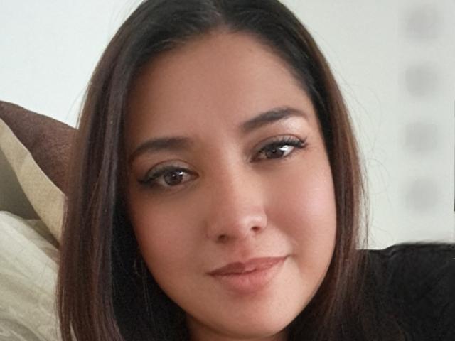 PaulaAnd has brown eyes, long dark brown hair, and a slight smile, with subtle makeup and a smooth, tan skin tone, looking directly at the camera.