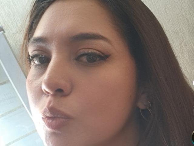 PaulaAnd has brown eyes, long brown hair, and wears black eyeliner with subtle eyelashes. She has a light brown skin tone and is pouting her slightly glossed lips.