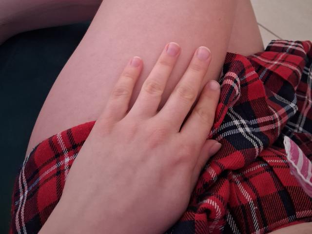 Marriam's hand rests on her bare thigh, wearing red plaid shorts. Her pink-nailbed fingers gently touch her smooth skin.
