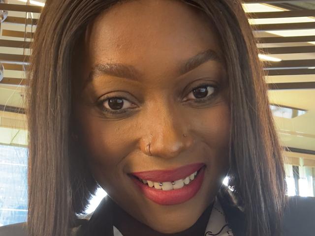 LaToyah's face with brown eyes, straight brown hair, nose ring, and pink lipstick smiling, showing white teeth. She's wearing a black and white patterned top.