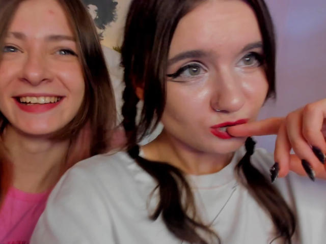 LuluMao con i capelli intrecciati, rossetto rosso e smalto nero, che si succhia il dito, accanto a LuluMao con i capelli castani lisci e una maglietta rosa, che sorride..
