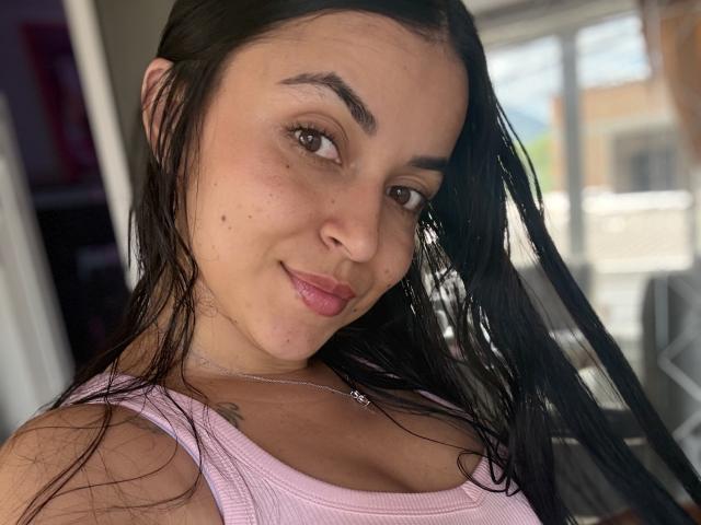 HikariChloe has wet black hair, brown eyes, and a slight smile. She's wearing a pink ribbed tank top, showing her small tits, and a necklace.