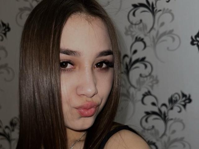 ShawneeLinderholm with pouty lips, brown eyes, and long brown hair, looking slightly to the side, wearing a black top, with a subtle silver necklace.